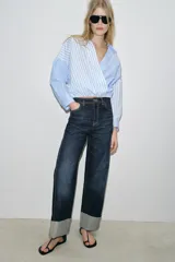 Camisa de popelín con estampado de rayas azules y blancas en diferentes direcciones, cuello solapa, escote pico cruzado, manga larga y bajo elástico.