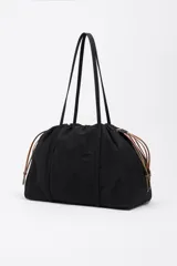 Bolso de hombro Bimba y Lola de tamaño grande, confeccionado en nylon negro con estructura blanda. Presenta dos asas largas, cierre superior y detalles de cordones laterales en tonos tierra. Incluye un parche frontal con el logo de la marca grabado.