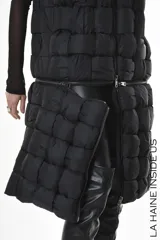 Chaleco puffer negro con diseño de cuadros, capucha y bolsillos laterales. Tiene cierre central y un cierre horizontal a la altura de la cadera que permite quitar la parte inferior, modificando el largo del chaleco.