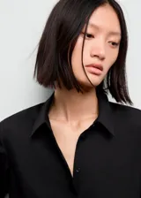 Camisa básica de tejido fluido y color negro, con diseño recto, cuello camisero, manga larga con puños abotonados y cierre delantero con botones.