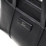 Cartera de mano y hombro color negro, con textura de cuero granulado. Presenta dos asas superiores y una correa larga regulable y desmontable. El frente lleva un aplique rectangular con el logo XL.