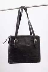 Cartera de hombro estructurada color negro, confeccionada en 100% cuero vacuno con textura en relieve tipo reptil. Cuenta con asas largas ajustables mediante hebillas metálicas plateadas, cierre superior y el logo de la marca grabado en la parte frontal.
