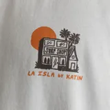 Remera verde con estampa en el pecho de una tienda de surf, palmeras y un atardecer.