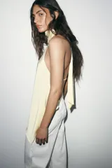 Top halter negro de tela satinada, con cuello drapeado y bajo asimétrico con caída.