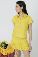 Top de lino color blanco, con cuello polo, cierre frontal parcial y mangas cortas. Presenta pespuntes a contratono.