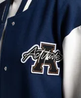 Campera bomber azul marino con mangas blancas, cuello, puños y ruedo acanalados con rayas blancas y azul marino. Tiene cierre frontal con botones a presión y un pequeño bordado en el pecho.