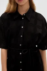 Vestido corto de algodón color blanco con diseño de broderie, cuello camisero, cierre frontal con botones, mangas cortas y lazo ajustable en la cintura.