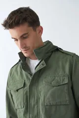Campera de gabardina verde militar con capucha desmontable y ajustable, cierre frontal con cremallera y múltiples bolsillos con solapa.