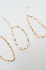 Set de cuatro brazaletes dorados con diferentes diseños: uno de eslabones tipo concha, uno con perlas engarzadas, uno de cadena fina y uno con eslabones en forma de espiga.