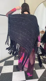Ruana tejida de color negro con sutiles destellos plateados, diseño de líneas verticales y terminación con flecos largos en los extremos.