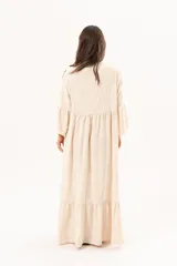 Vestido largo beige de silueta oversize, confeccionado en tela ligera con textura y motivos bordados tono sobre tono. Presenta escote en V, mangas amplias con volados y un gran volado en el ruedo.