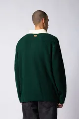 Sweater de punto con textura waffle en color blanco, con cuello polo en contraste color verde oscuro y cierre frontal de botones. Presenta un bordado decorativo en el pecho y un corte relajado.