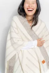 Ruana color crudo con diseño tejido a rayas verticales en tonos beige y flecos en el borde inferior.