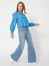 Camisa celeste de corte cropped, sin cuello, con mangas largas abullonadas y puños con botón.