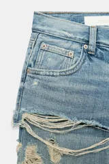 Jeans de tiro bajo y corte recto, color celeste con efecto lavado. Presenta diseño de doble tiro con detalle de short superpuesto con roturas, además de roturas adicionales en las perneras. Cuenta con cinco bolsillos, trabillas para cinturón y cierre frontal con cremallera y botón metálico.