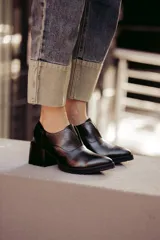 Zapato de cuero color beige, con taco de madera y suela dentada. Presenta un diseño slip-on con detalles de textura en relieve en los laterales y el empeine.