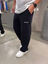 Pantalón de jogging negro de corte holgado, con cintura elástica y bolsillos laterales. Presenta un pequeño logo bordado en blanco en la parte superior izquierda.