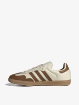 Championes Adidas modelo Samba OG, con exterior de cuero premium en color crema y detalles en marrón, suela de caucho y diseño clásico de inspiración futbolística.
