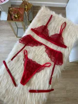 Conjunto de lencería de tres piezas en encaje rojo, compuesto por un bralette triangular, una tanga regulable y un portaligas con volados en las caderas.