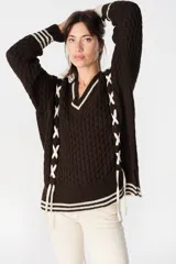 Sweater de punto trenzado color marrón con cuello en V y detalles de cordones cruzados en color crudo a los costados. Presenta puños con rayas en contraste y cuello con borde en color crudo.