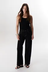 Musculosa negra ajustada al cuerpo con escote redondo y tirantes finos. Presenta un detalle metálico en forma de aro o hebilla en la unión del tirante con el cuerpo de la prenda.