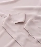 Blusa de crepé color rosa pálido, con cuello redondo, mangas cortas con volados, lazo en la cintura y botón en la espalda.