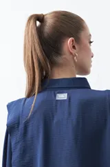 Camisa negra de estilo sastrero con cuello clásico, frente abotonado y mangas largas con puños ajustados. Presenta un diseño con hombreras sutiles que aportan estructura a la prenda.