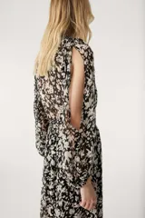 Vestido largo de gasa color negro con estampado floral blanco, escote en V cruzado, mangas largas con aberturas en los hombros y falda con volantes.