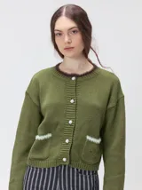 Cardigan de algodón grueso color verde oliva, con cuello redondo, cierre frontal con botones decorativos, bolsillos frontales con detalle de pelo sintético y logo bordado en el bolsillo izquierdo.