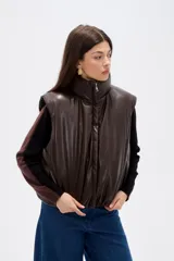 Chaleco acolchado de cuero sintético en color marrón oscuro, con cuello alto, cierre frontal y diseño holgado.