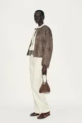 Chaqueta bomber color marrón con cuello redondo, manga larga con puño elástico y cierre frontal de cremallera metálica. Presenta un diseño de bordados florales en relieve por toda la prenda y bolsillos delanteros de vivo.