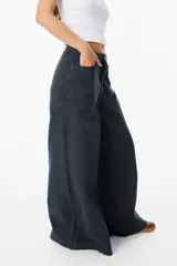 Jean de corte wide leg en color negro lavado, con tiro medio y cierre de botón y cremallera. Presenta bolsillos traseros amplios y etiqueta de cuero sintético con el logo de la marca en la parte posterior.