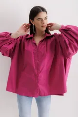 Camisa fucsia de algodón, corte holgado, con cuello camisero, cierre frontal con botones y mangas largas abullonadas con puños abotonados.