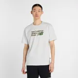 Remera gris jaspeado de manga corta, corte holgado y cuello redondo. Estampado frontal con el logo de New Balance y la leyenda "athletic shoes" en verde.