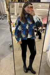 Camisa de popelina con estampado artístico multicolor, cuello clásico y cierre frontal con botones. Presenta un diseño con fruncido lateral tipo corset, mangas abullonadas y cordones decorativos en los costados.