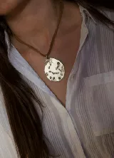 Collar con dije de alpaca en forma de gota irregular con textura grabada, montado sobre un cordón de cuero marrón.