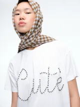 Remera blanca de corte oversize con la palabra 'Cute' escrita en el frente mediante apliques de strass brillantes.