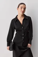 Camisa blanca de manga larga con textura suave y caída liviana, cuello camisero, puños anchos y fruncidos sutiles en los hombros.