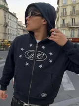 Canguro negro con cierre frontal, capucha y bolsillos tipo canguro. Presenta un estampado frontal en color blanco con un diseño ovalado rodeado de estrellas.