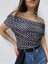 Top de bikini o crop top negro con estampado de lunares blancos, escote bardot (hombros descubiertos) y mangas cortas.