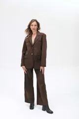 Blazer de ante color marrón con silueta oversize, cierre frontal con botones, bolsillos con solapa y tajo trasero. Presenta detalles de costuras con terminaciones pintadas a mano.