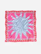 Pañuelo cuadrado de tela liviana con diseño gráfico central de sol en tonos celeste y fucsia, rodeado por un borde estampado con motivos de soles y texto repetitivo. Presenta el logo de la marca en una esquina.