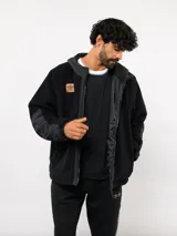 Campera de polar negra con capucha, cierre frontal completo y detalles en nylon en mangas y bordes. Presenta un parche con el logo de Umbro en el pecho.
