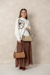 Cartera tipo baguette de diseño minimalista, confeccionada en una combinación de gamuza color beige en el panel frontal y cuero color chocolate en los bordes y la correa. Incluye un detalle colgante de cuentas de madera y cierre superior.