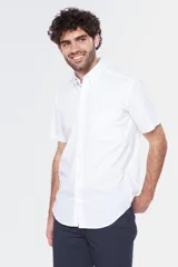 Camisa de manga corta color celeste claro, con cuello abotonado (button-down) y un bolsillo de parche en el pecho.