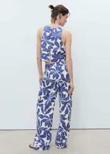 Pantalón tiro medio de corte recto, con estampado floral azul sobre fondo blanco, detalle de pinzas y bolsillos laterales. Cierre oculto con botón, gancho y cremallera.