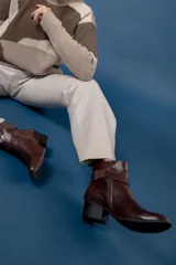 Bota corta de cuero negro con acabado brillante, punta redondeada y taco cuadrado bajo. Presenta una tira decorativa en el tobillo con una hebilla metálica plateada grande.