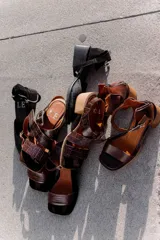 Sandalias de cuero negro con textura de reptil, diseño de punta cuadrada y taco bloque de madera. Presentan tiras cruzadas en el empeine y una hebilla metálica grande decorativa.