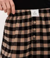 Pantalón de pijama de corte holgado confeccionado en franela con estampado de cuadros en tonos beige y negro. Presenta cintura elástica con botones decorativos en la parte frontal.