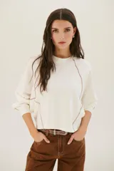 Buzo negro de corte cropped con mangas largas abullonadas y costuras a la vista en color blanco.